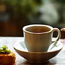 Photo d'une tasse de café et d'un financier à la pistache de Jardin Gourmand sur une table de café parisien, ambiance chaleureuse.